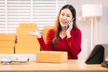 A smiling woman, who appears to be a middle-aged Asian individual, stacks cardboard boxes on a desk...
