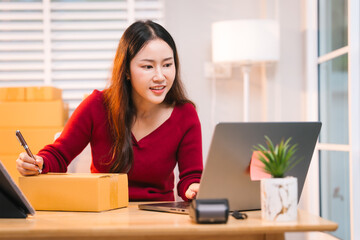A smiling woman, who appears to be a middle-aged Asian individual, stacks cardboard boxes on a desk...
