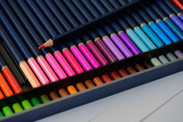 Two rows of colored pencils with a sharp point on red pencil in pencil case. Big beautiful color palette watercolor pencils for creativity drawing, close-up, high resolution.