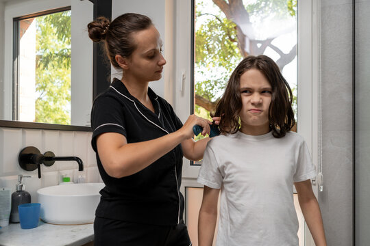 Mother patiently provides long hair care, combing her son's locks despite his grumpy scowl and annoyed sideways glance. This daily routine highlights detangling challenges and mom's dedicated care.