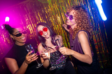 Happy women friends toasting with champagne celebrating at disco party