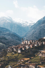 view of a small village from the top of the mountain, pale light, haze and snowy peaks background on an early spring day