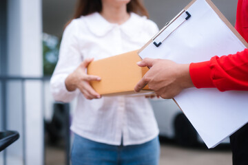 Attractive Asian delivery man in a red uniform hands a package to a middle-aged woman who is...