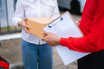 Attractive Asian delivery man in a red uniform hands a package to a middle-aged woman who is...