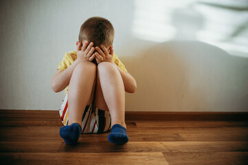 Little boy lonely depressed sitting on floor in the room close eyes hand. autism spectrum disorder, psychological problems, mental health. associative behavior, no contact. Children stress of divorce 