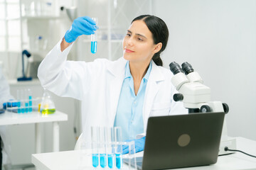 Fototapeta premium A scientist and researcher laboratory examines test tube with blue liquid, surrounded by lab equipment like microscope and laptop, showcasing chemistry work scientist researcher chemistry laboratory
