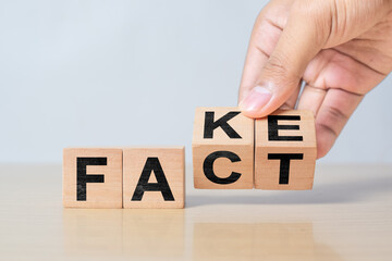 Fact or fake concept. Human hand flips wooden block to switch between fact and fake text. Symbol of truth, doubt, and information accuracy.