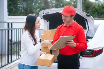 A delivery man, who appears to be Asian, in a red uniform shows a clipboard to a smiling woman, who...