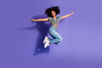Energetic young woman jumps with joy on a vibrant purple background, stylish and casual in her...