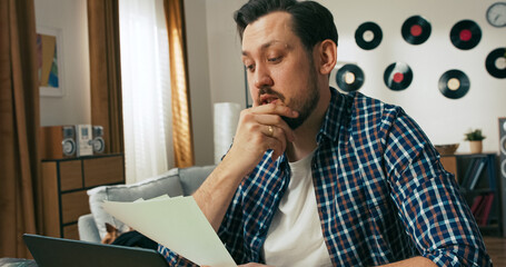 A confused and frustrated young man with a disability sits at home reading bills and debt...