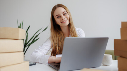 Fototapeta premium Young woman working at a desk with a laptop surrounded by packages
