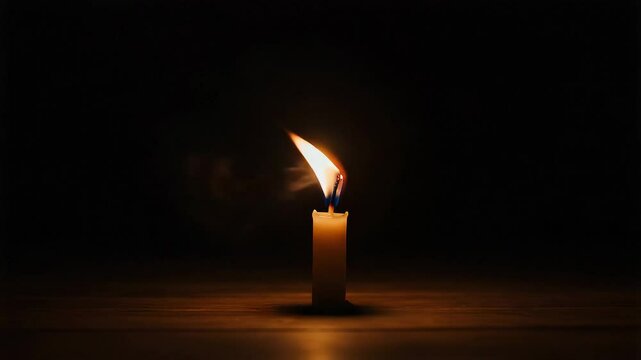 Candle flame flickering in darkness with wind blowing over it  