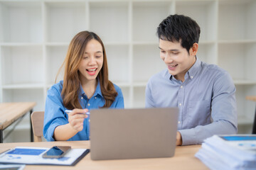 Two young asian businesspeople are smiling and working together using a laptop computer in the...