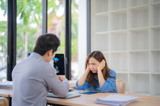 Stressed businesswoman covering ears with hands while listening to her male colleague explaining bad results during a business meeting in the office