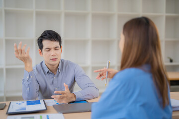 Fototapeta premium Two asian businesspeople discussing about negative financial report, businessman is stressed and gesturing with hands while having a difficult conversation with his colleague