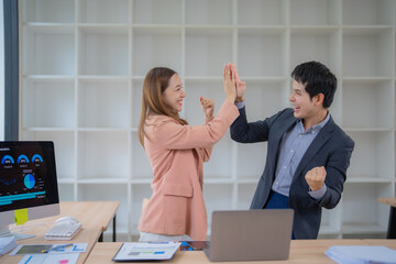 Two Asian businesspeople celebrating a successful project meeting, smiling and giving each other a high five in a modern office environment