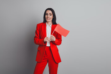 Successful businesswoman in a red suit holding a small red flag against a grey background...