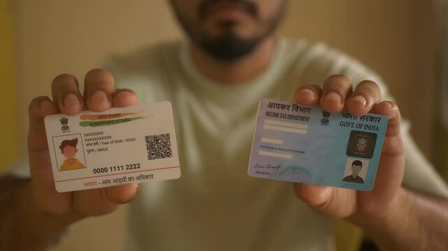 Indian nationality man holding PAN card from Income Tax Department and Aadhaar card, government programmes, closeup