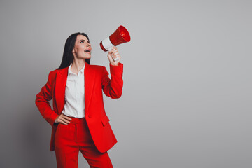 Confident businesswoman in a red suit holding a megaphone in an office setting with a professional grey background
