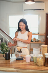 Asian woman preparing pour over coffee with fresh beans and mugs on the counter