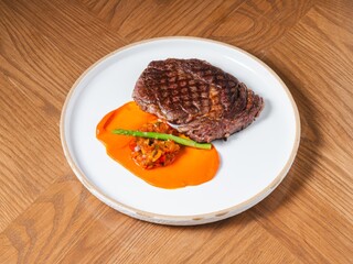 Grilled beef steak with sweet pepper sauce and asparagus on white ceramic plate