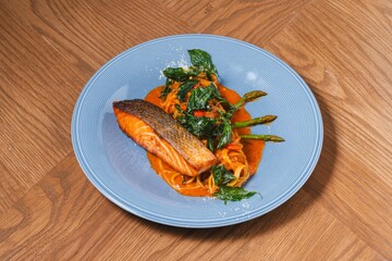 Grilled salmon fillet with red curry pasta and crispy Thai herbs on blue plate