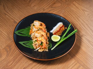 Pad Thai with prawns served on black ceramic plate with lime and seasonings