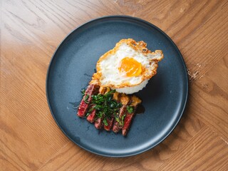 Thai beef basil with rice and crispy fried egg on black plate