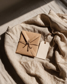 Wrapped parcel and blank tag on a linen fabric in sunlight, rustic presentation.