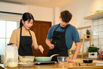 Happy young couple in aprons preparing to cook pancakes in a cozy home kitchen