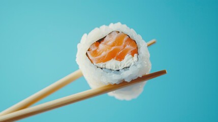 Sushi roll with salmon and cream cheese held by chopsticks on blue background