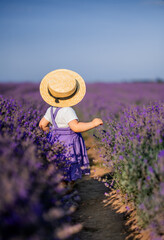 little girl child in a lilac sundress and a braided hat stands in a field of lavender