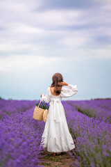 girl in a white dress stands in a field of lavender with a basket of flowers