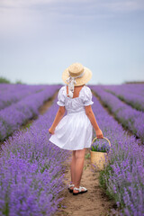 girl in a white dress and hat stands in a field of lavender with a basket of flowers