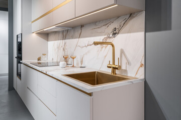 design of large built-in kitchen is white with gold elements, marble countertop, golden faucet and...
