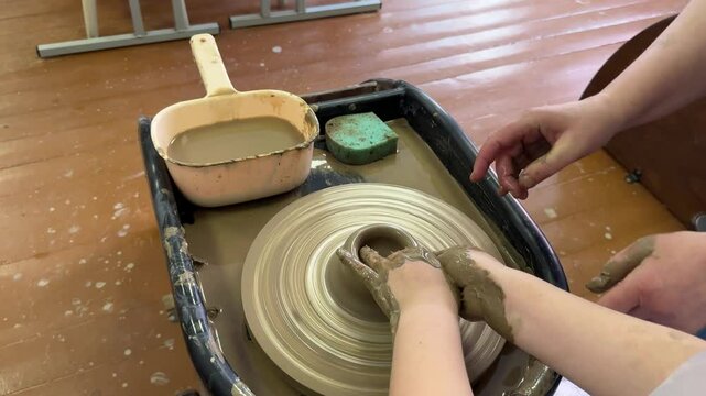 potter teaches the child. A craftsman sits on a bench with a potter's wheel and makes a clay pot.