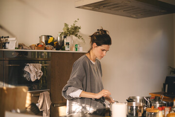 Woman standing by the stove in the kitchen, cooking and smelling the nice aromas from her meal in a pot. Housewife cooking lunch or breakfast.