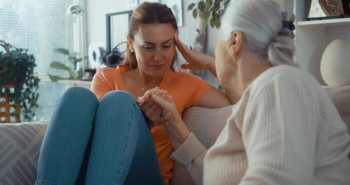 Wise older mother or grandmother offers heartfelt comfort and advice to her crying daughter or granddaughter in living room. Multi-generational family connection. Motherly advice for an adult daughter
