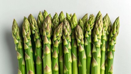 A close-up, top-down view of vibrant, fresh green asparagus spears with their tips pointing upwards, arranged uniformly against a light background, highlighting their natural beauty and crisp texture.