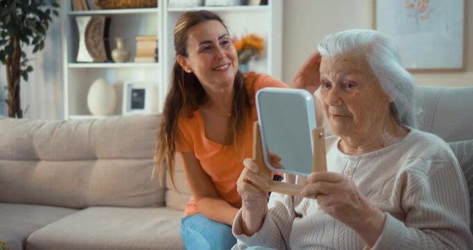 A satisfied 90s woman reflects in the mirror after receiving beauty care hair from her adult daughter at home.