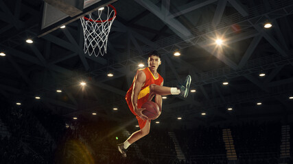 Conceptual collage. Basketball player jumps high holds ball under basket on 3D arena with lights and visible metal roof structure. Concept of sport, movement, competition, championship, tournament.