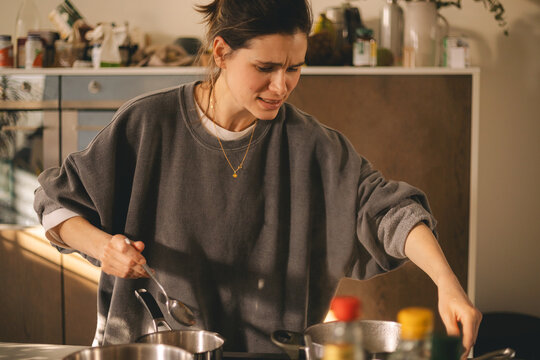 Young housewife having a calamity in the kitchen reacting in shock, she cooks dinner. Woman in a hurry, look sad and mad.
