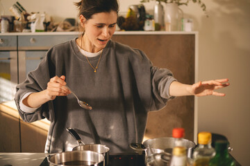 Young housewife having a calamity in the kitchen reacting in shock, she cooks dinner. Woman in a hurry, look sad and mad.