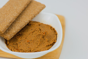 A close-up on a wooden board is a white plate with liver pate, slices of bread on top of it on a white background. The concept of healthy food, a healthy snack. High quality photo