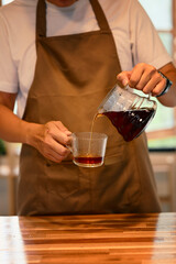 Cropped shot of man pouring fresh brewed coffee into glass cup in a kitchen