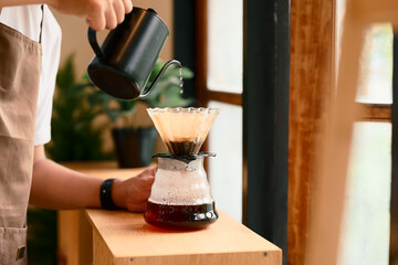 Close up of man brewing coffee with pour over method using a glass dripper in a kitchen