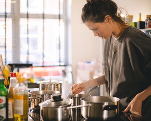 Woman standing by the stove in the kitchen, cooking and smelling the nice aromas from her meal in a pot. Housewife cooking lunch or breakfast.