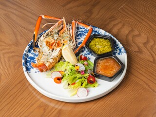 Grilled river prawn with spicy seafood sauce and salad on ceramic plate