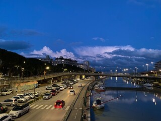 Twilight view of the Lungofiume dei Poeti in Pescara, Italy, with cars driving and boats moored in the canal
