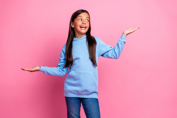 Charming young girl in blue hoodie posing on pink background showcasing casual style and gestures of curiosity and happiness.